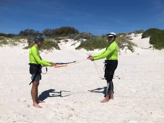 An Actionsportswa Kitesurf instructor shows a student safety control bar systems on a sandy beach